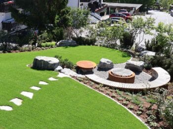 Neu gestalteter Garten mit großer Rasenfläche, Natursteinen, runder Feuerstelle und geschwungener Holzbank